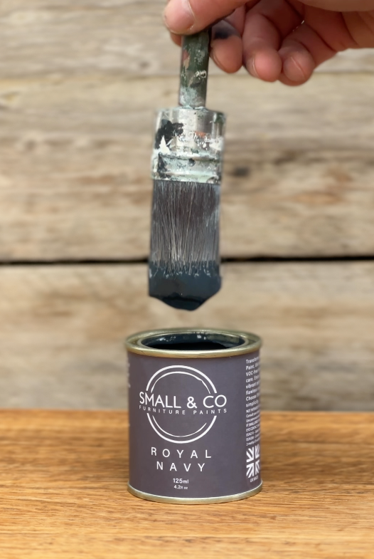 Close-up of paintbrush dipped into Small & Co Royal Navy furniture paint tin, beginner guide to applying the first thin coat for smooth DIY finish
