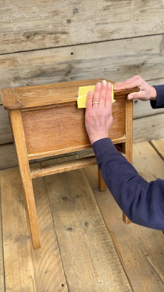 Beginner lightly sanding wooden furniture before painting using fine-grit sandpaper, part of step-by-step guide to preparing furniture for chalk paint